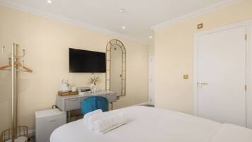 Quarto de hotel com cama, escrivaninha com cadeira, televisão, armário e cabideiro.