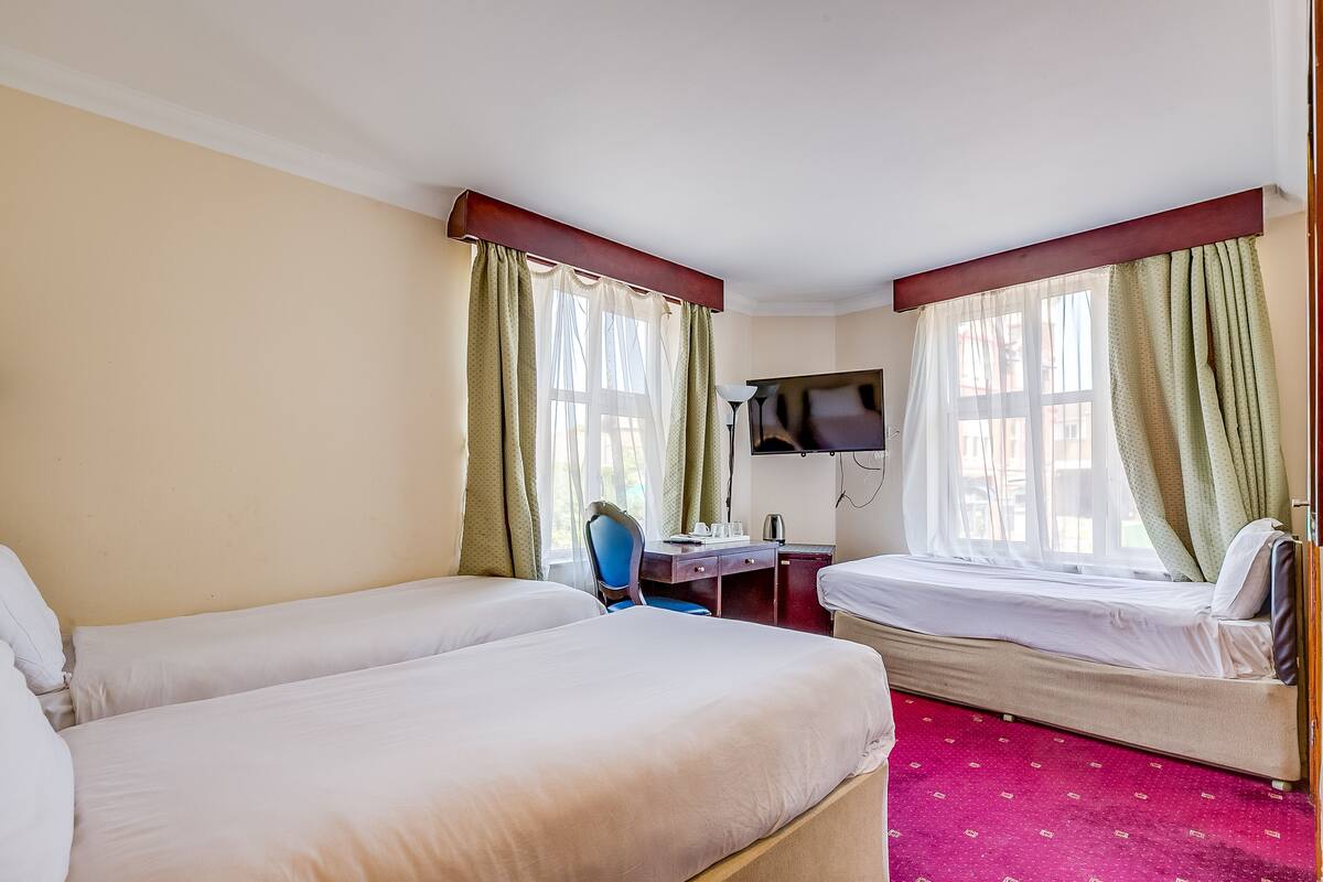 A hotel room with two single beds, a desk, a chair, a TV, and a window with curtains.