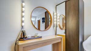 A modern bathroom with a vanity, a round mirror with lights, a wooden cabinet, and a white chair. - London Star Hotel (London)