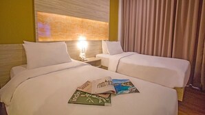 Habitación de hotel con dos camas, una mesita de noche con lámpara y vista al mar a través de amplias ventanas.