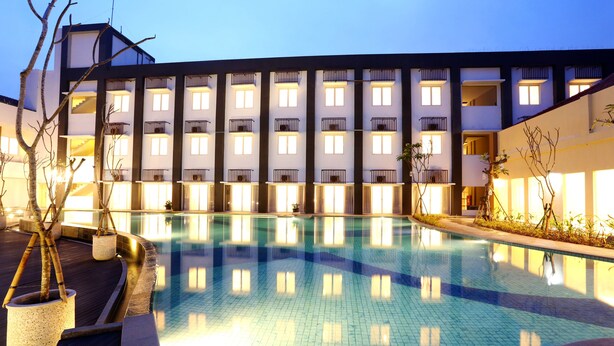 Un hotel con piscina, varios balcones y un diseño arquitectónico moderno.