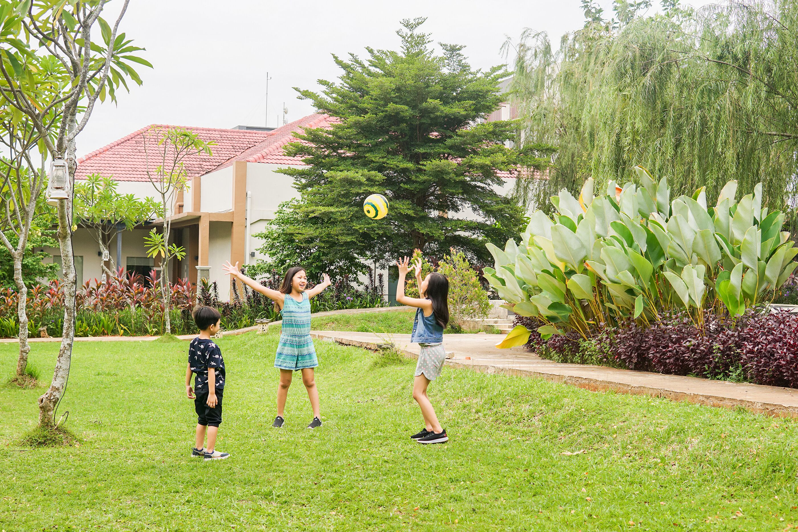 Tres niños jugando con una pelota en un área cubierta de césped, con un edificio al fondo.