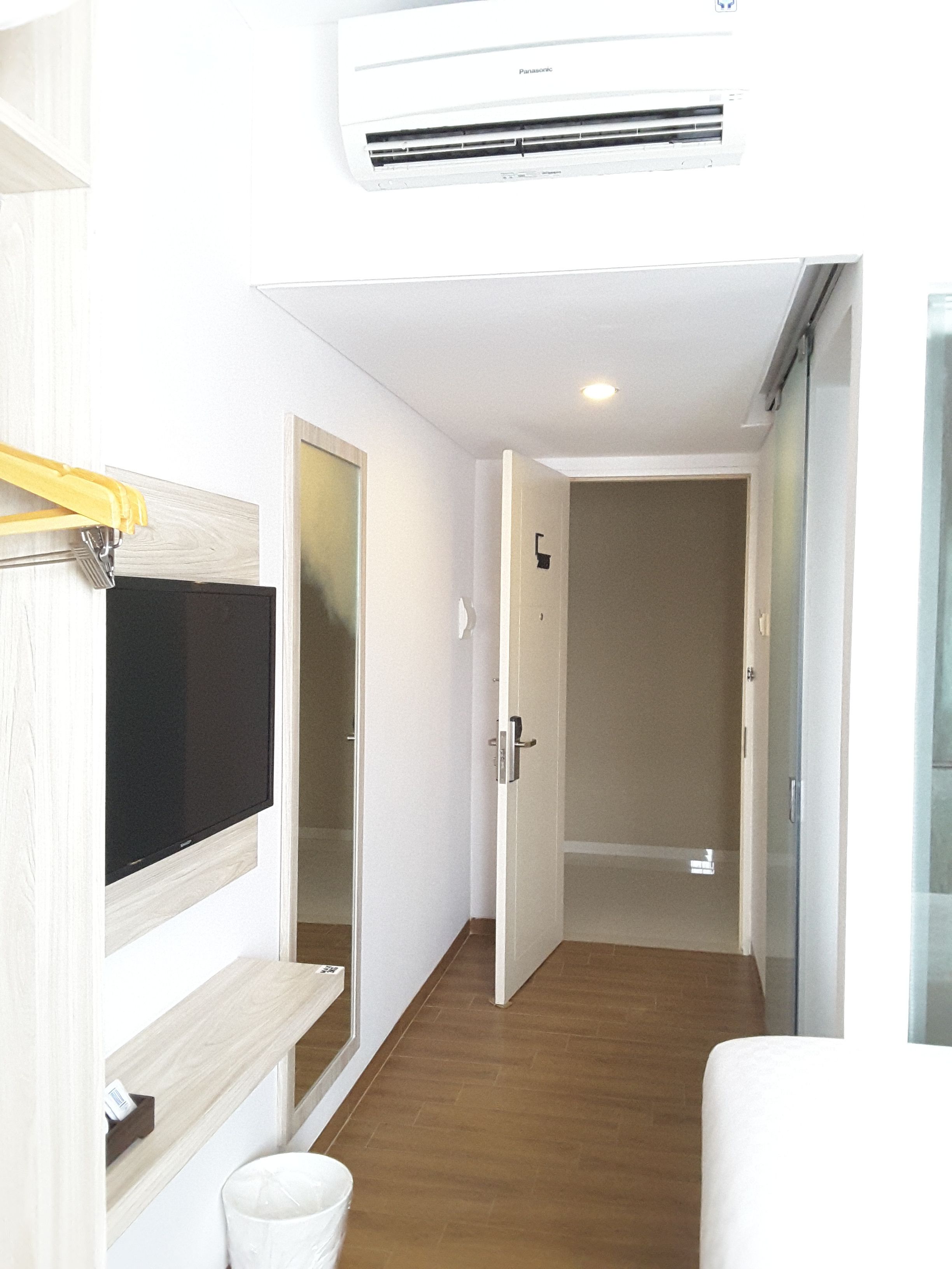 Habitación de hotel con una televisión de pantalla plana montada en la pared, suelo de madera y un equipo de aire acondicionado blanco sobre la puerta.