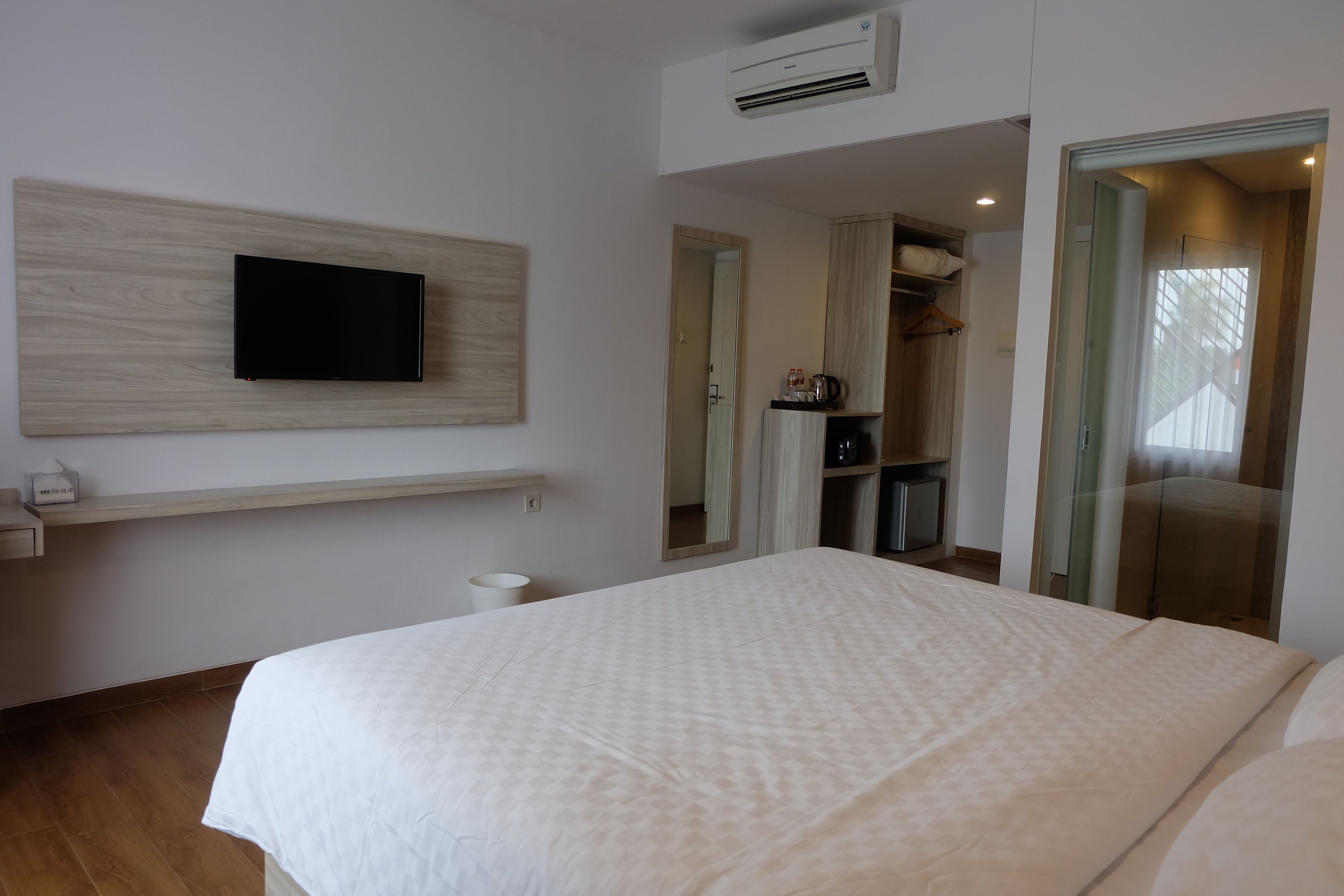 Et moderne hotelværelse med en stor seng, et ophængt fjernsyn, et lille skrivebord med elkedel og et garderobeskab.
