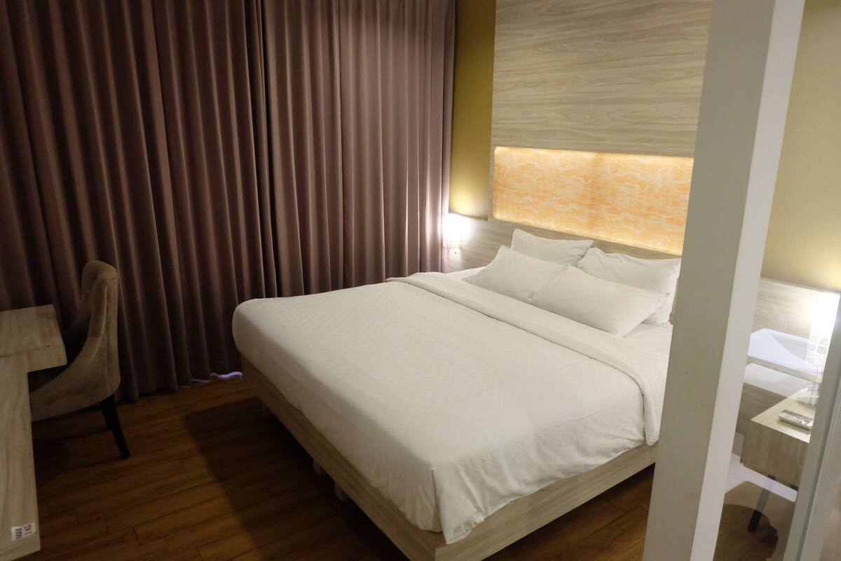 Een hotelkamer met een groot bed, een bureau met stoel en een raam met gordijnen.