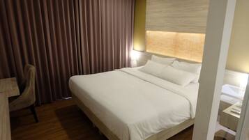 A hotel room with a large bed, a desk with a chair, and a window with curtains.