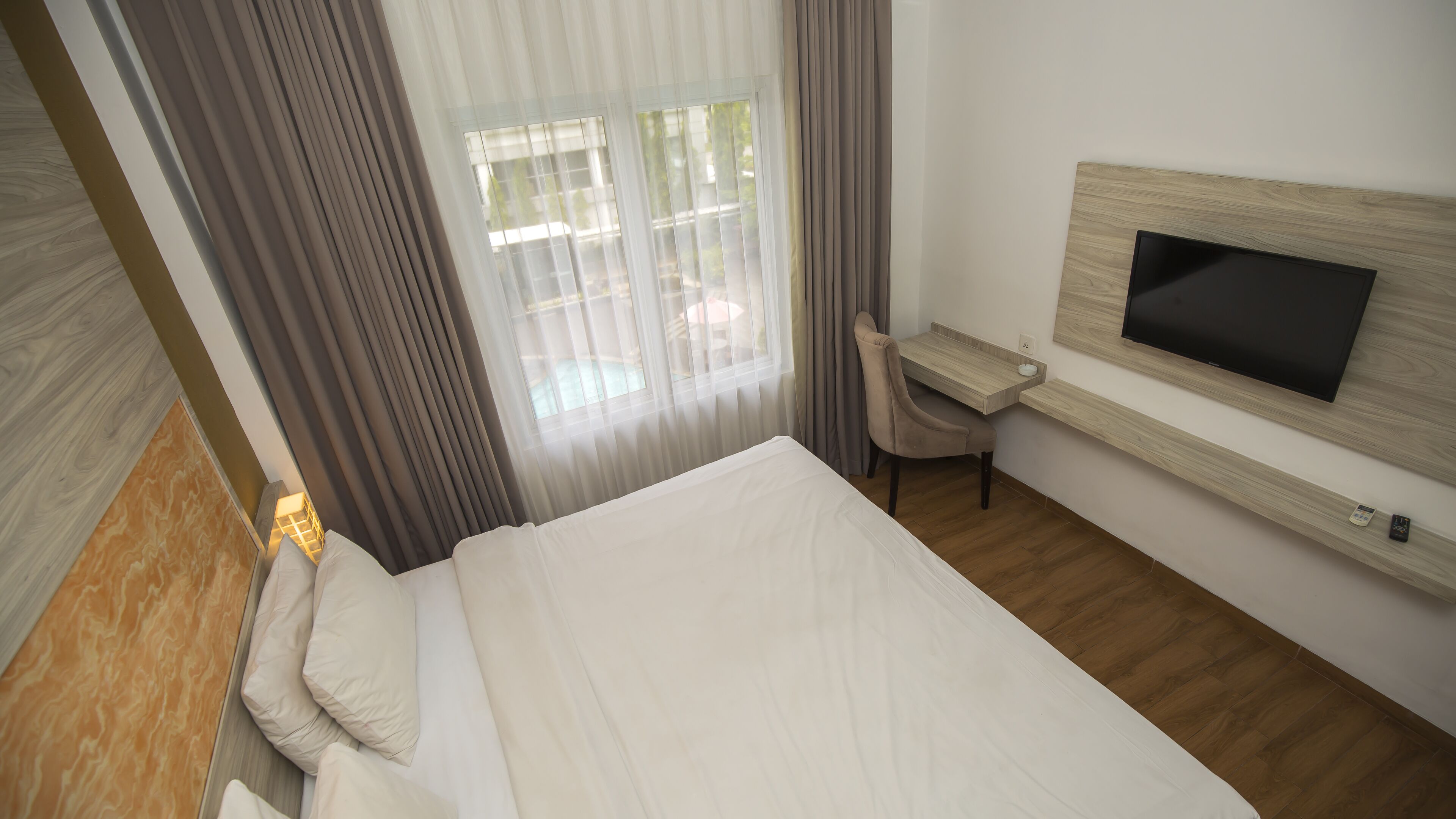 A hotel room with a bed, a desk, a chair, a TV, and a window with curtains.