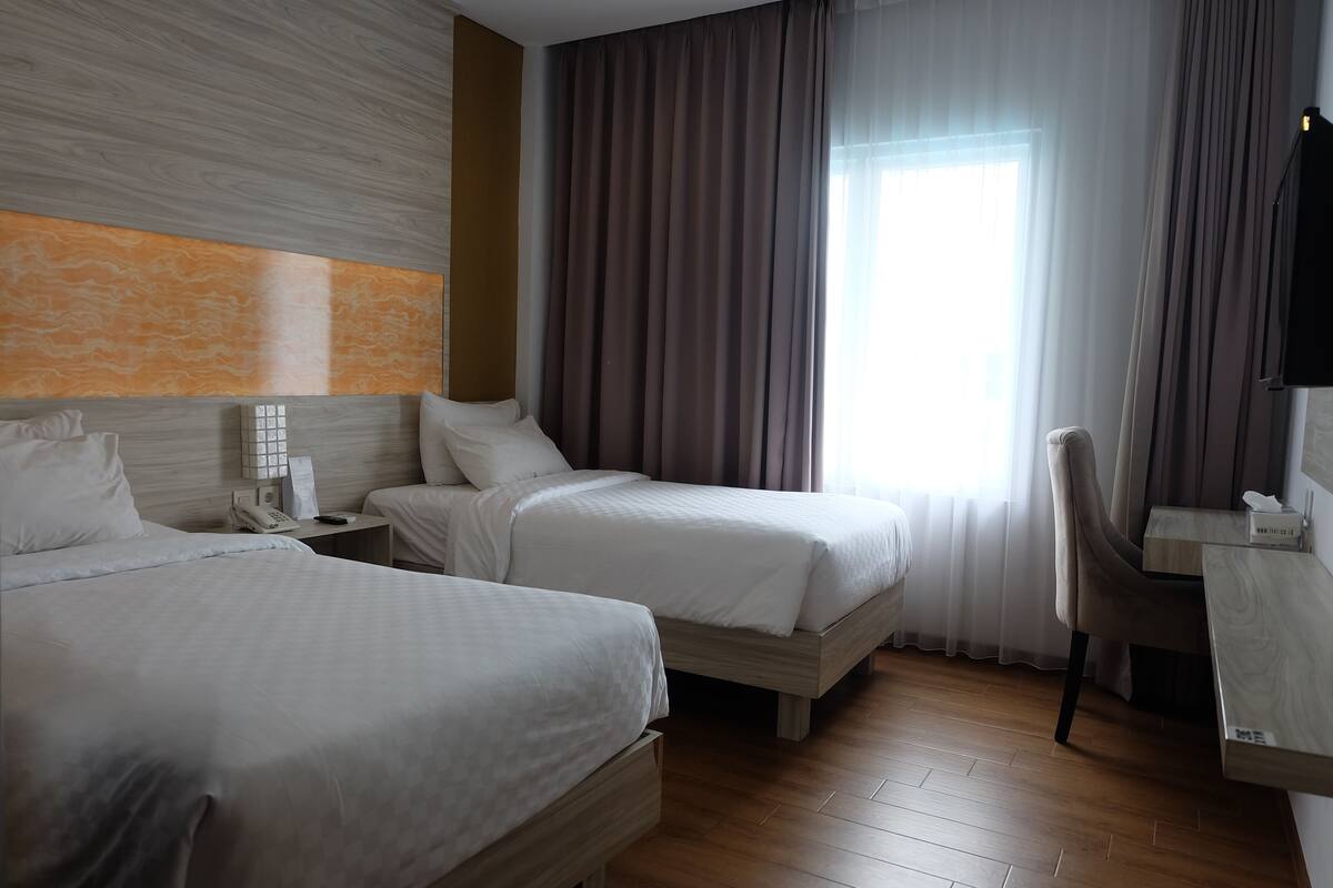 Een hotelkamer met twee bedden, een bureau, een stoel, een telefoon en een raam met gordijnen.