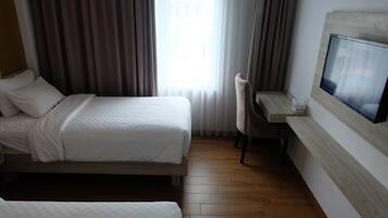 A hotel room with two beds, a desk with a chair, a TV, and a large window with curtains.