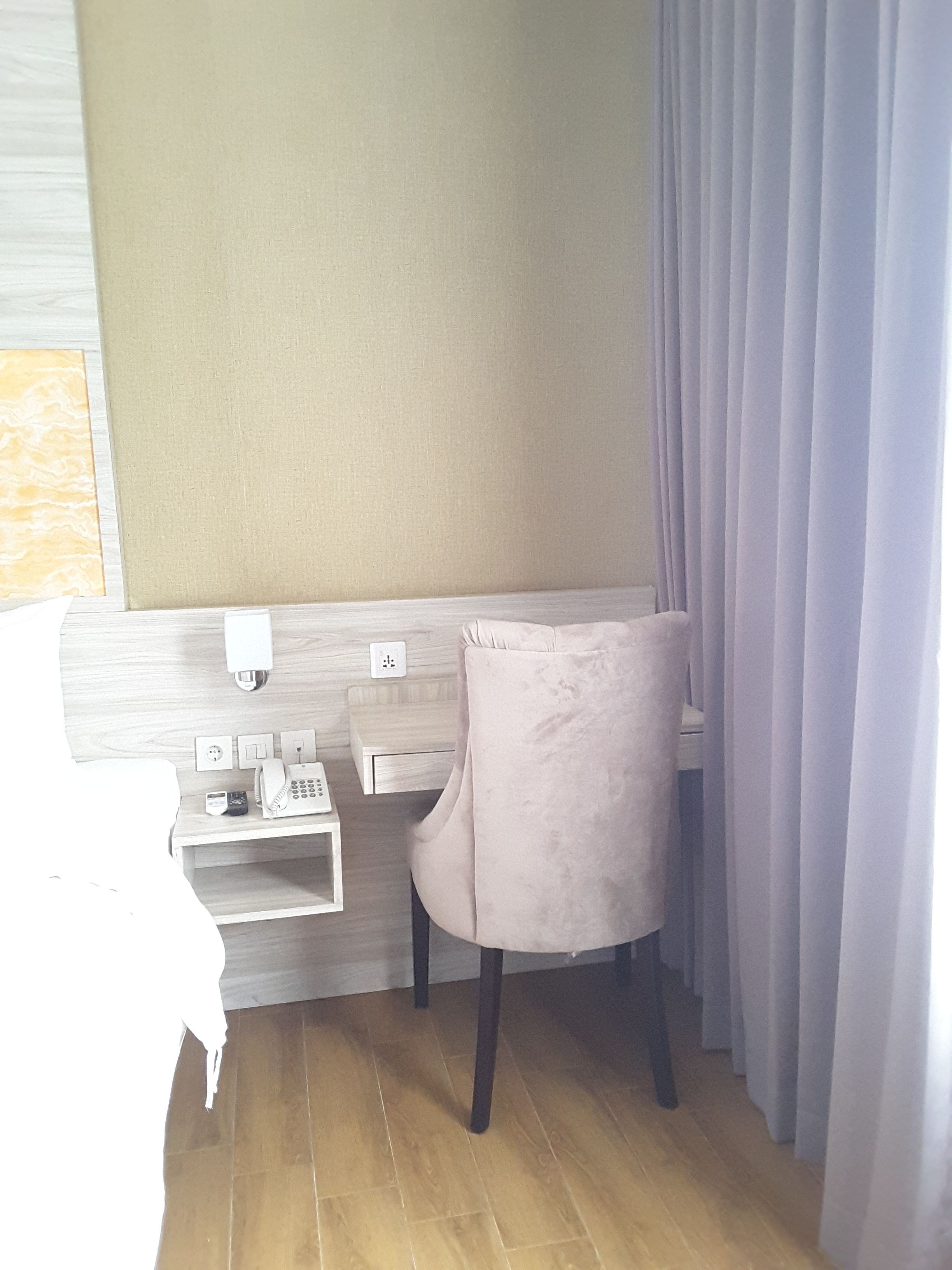 A corner room with a bed, a desk with a telephone, and a chair.