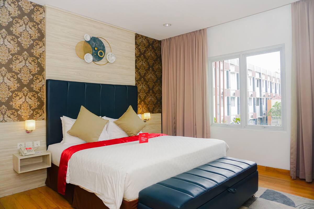 Een hotelkamer met een groot bed, een hoofdeinde met een klok, een nachtkastje met een telefoon en een raam met gordijnen.