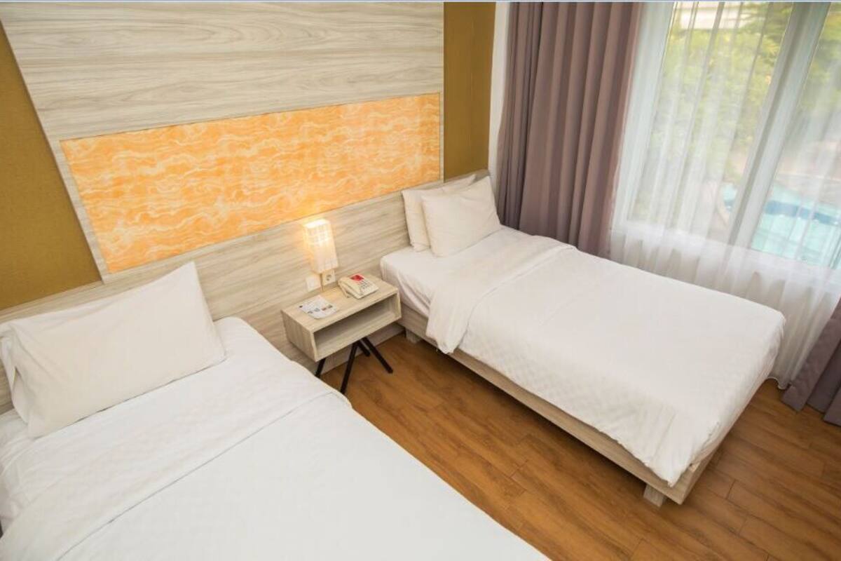 Een hotelkamer met twee eenpersoonsbedden, een nachtkastje met een lamp en uitzicht op een zwembad door het raam.
