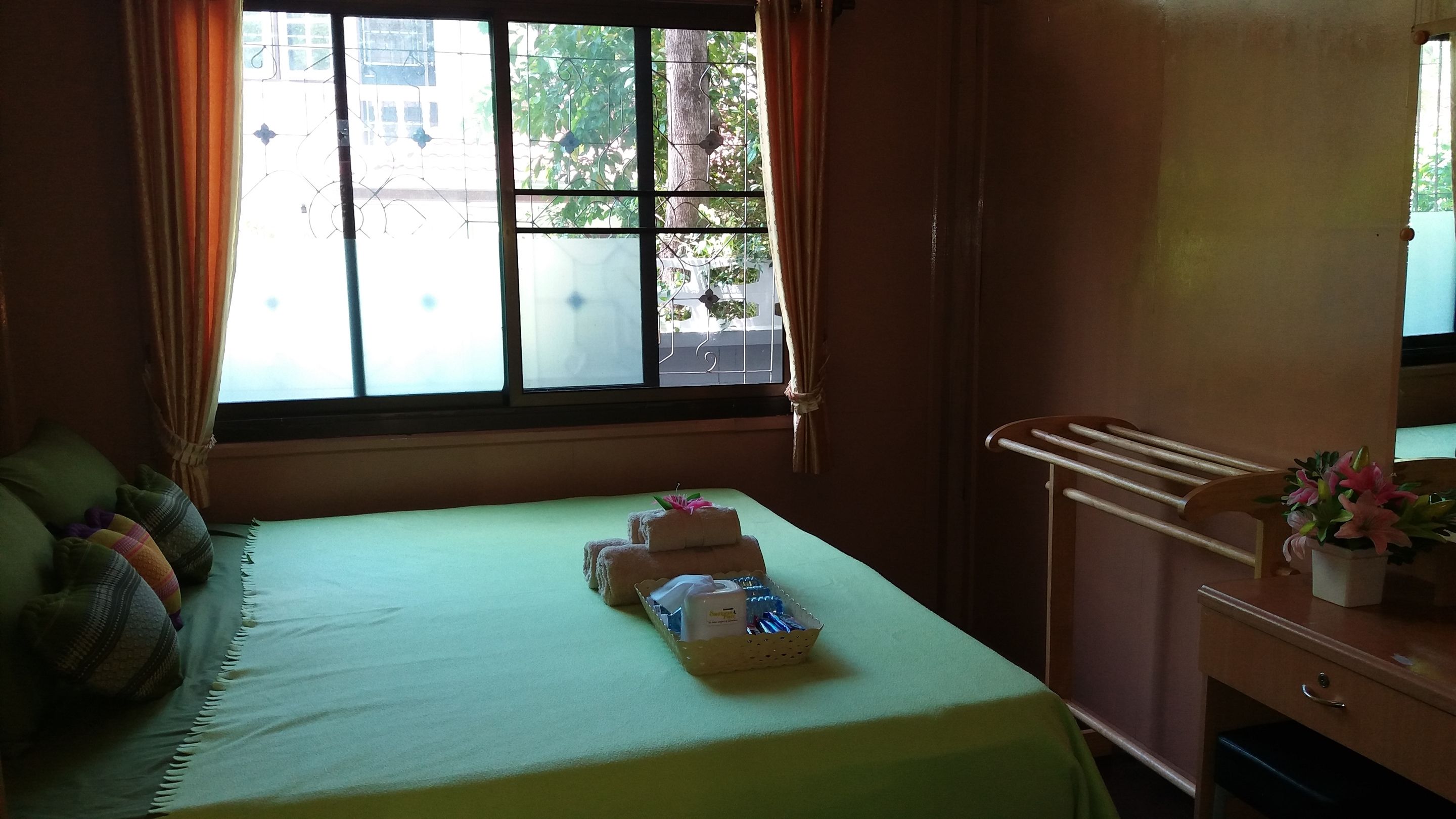 A hotel room with a bed, a window with curtains, a bedside table with a vase of flowers, and a towel rack.