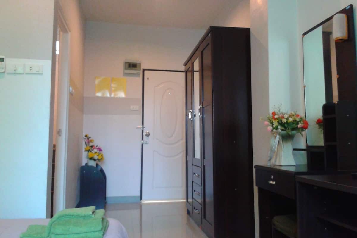 Una habitación de hotel con una cama, un armario, un escritorio con espejo y un florero con flores.