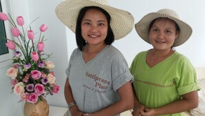 Deux personnes se tiennent à l’intérieur, l’une porte un t-shirt gris et l’autre un t-shirt vert ; les deux portent un chapeau de paille.