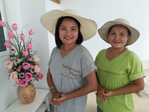 Two people standing indoors, one wearing a grey shirt and the other a green shirt, both with straw hats.