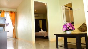 Une chambre d’hôtel avec un lit, une table ornée de fleurs, un miroir et une salle de bain visible à travers une porte ouverte.