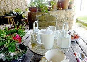 A rustic outdoor dining area with a wooden table set for tea, surrounded by potted plants and a stone wall. - La Casona Azul (Corvera de Toranzo)