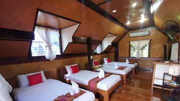Habitación de hotel con cuatro camas, cada una con sábanas blancas y almohadas rojas, cabeceros de madera y un ventilador de techo.