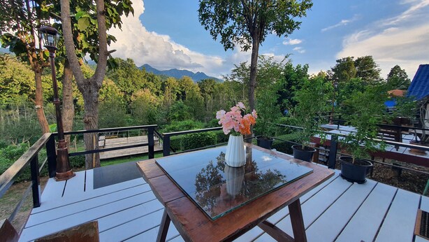 A wooden deck with a glass table and chairs, surrounded by lush greenery and a mountain backdrop. - Banphu Montalang Resort (Mae Hong Son)