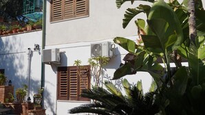 Un edificio de dos pisos con persianas marrones, unidades de aire acondicionado y plantas en macetas.