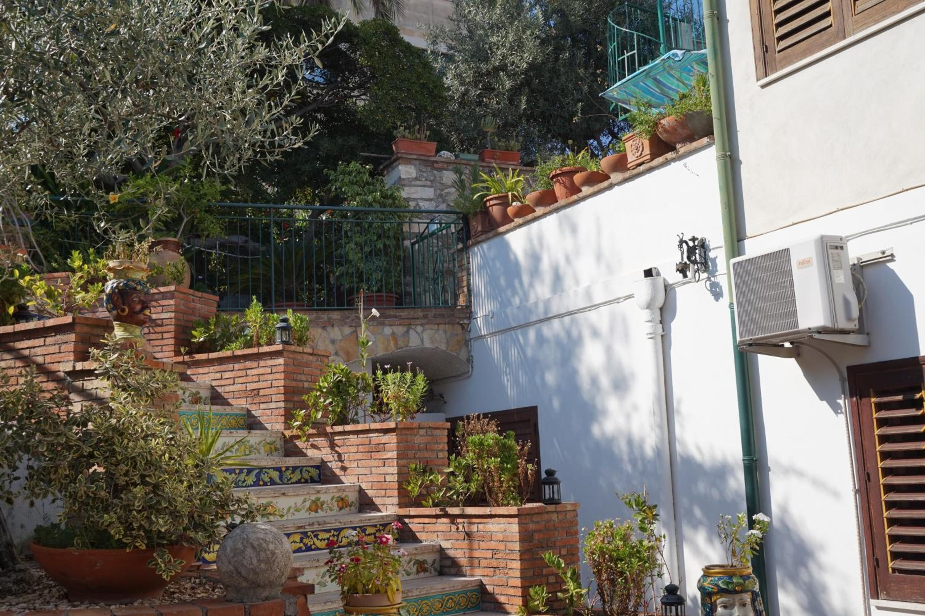 A courtyard with a staircase, potted plants, and a white building with a brick wall.