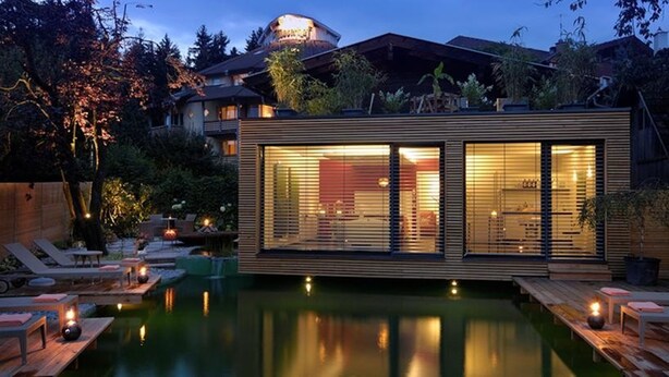 Een moderne woning met zwembad, houten terras en buitenmeubilair.