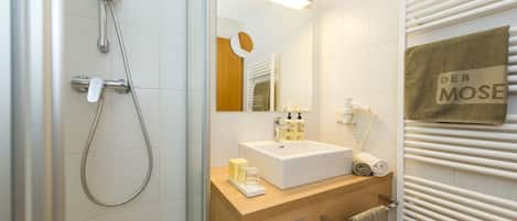 A modern bathroom with a shower, sink, mirror, towel rack, and a towel with "DER MOSE" on it.