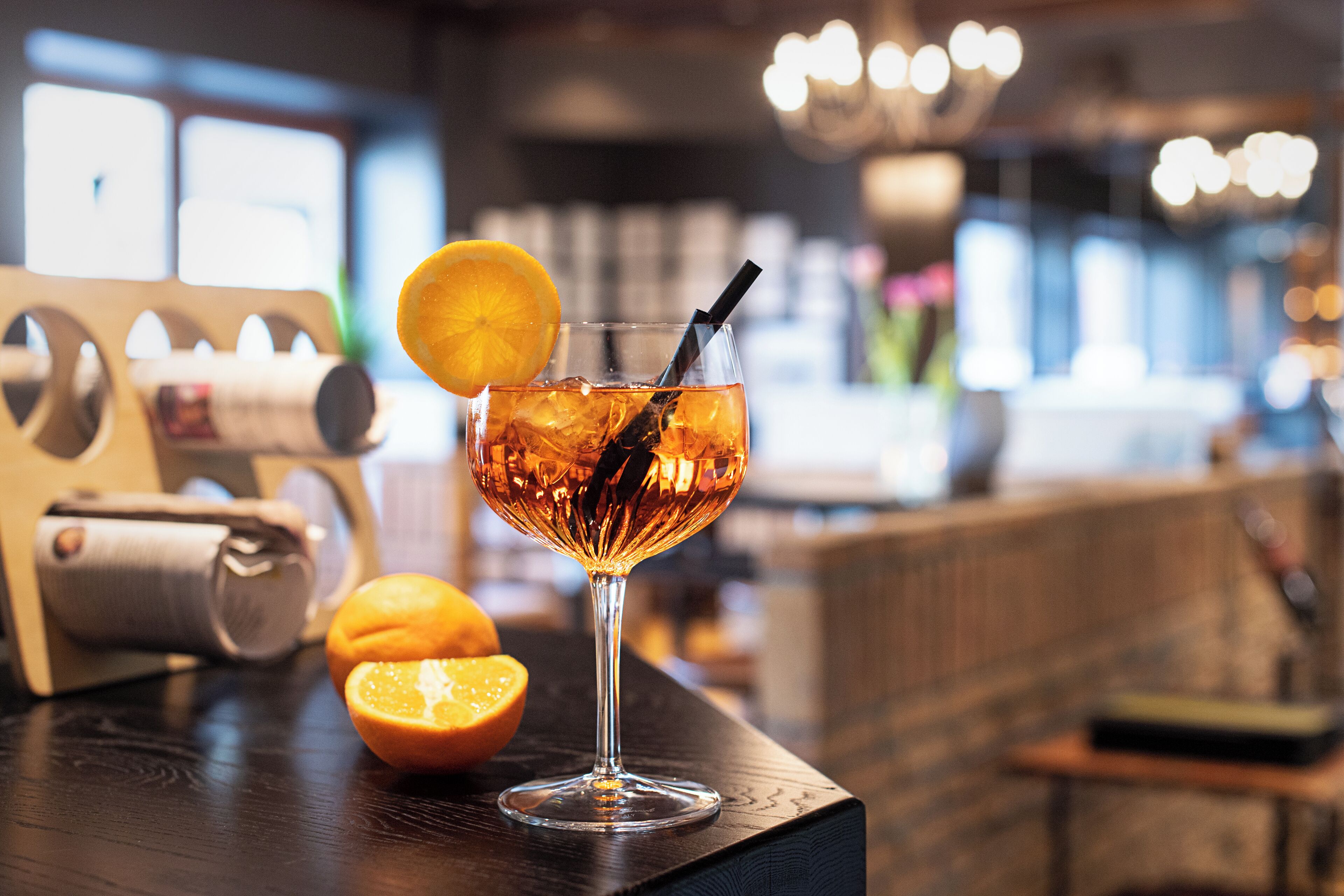 Een cocktailglas met een citroenpartje en een rietje op een houten bartafel.