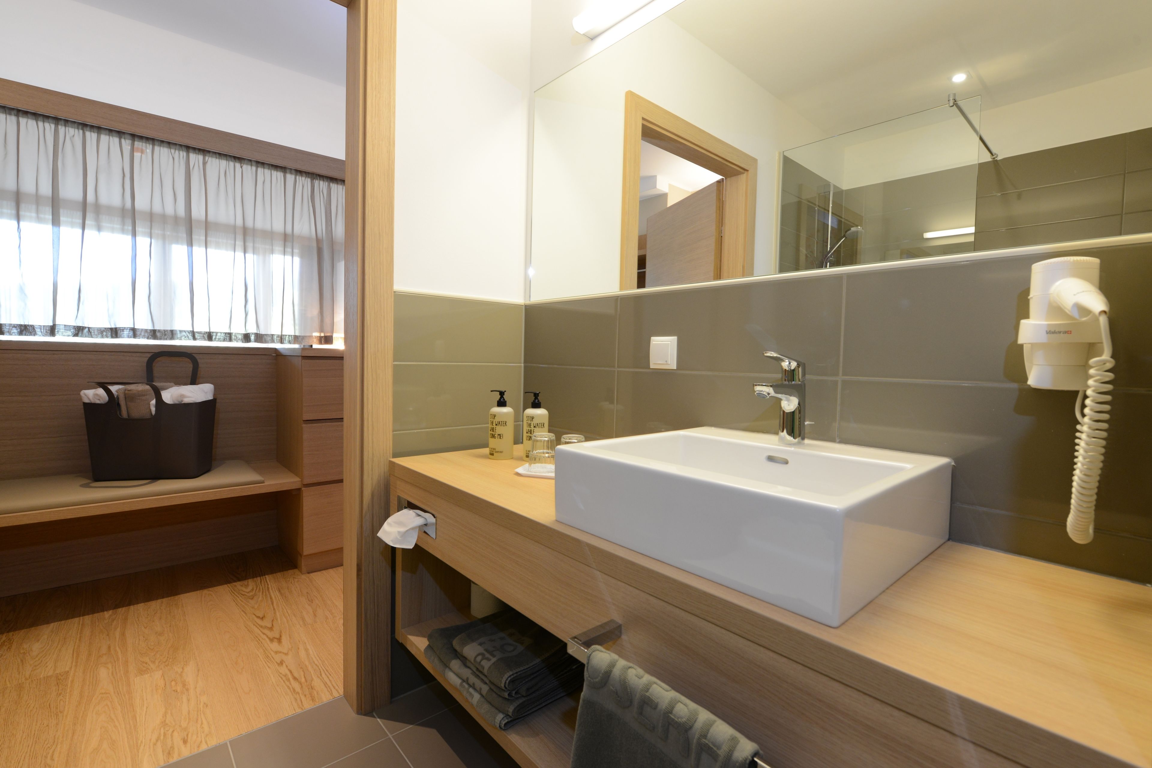 Un baño moderno con un espejo grande, un lavamanos blanco y un perchero para toallas.