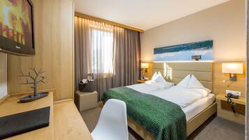 Habitación de hotel con cama, escritorio, silla, mesita de noche, lámpara y un cuadro en la pared.