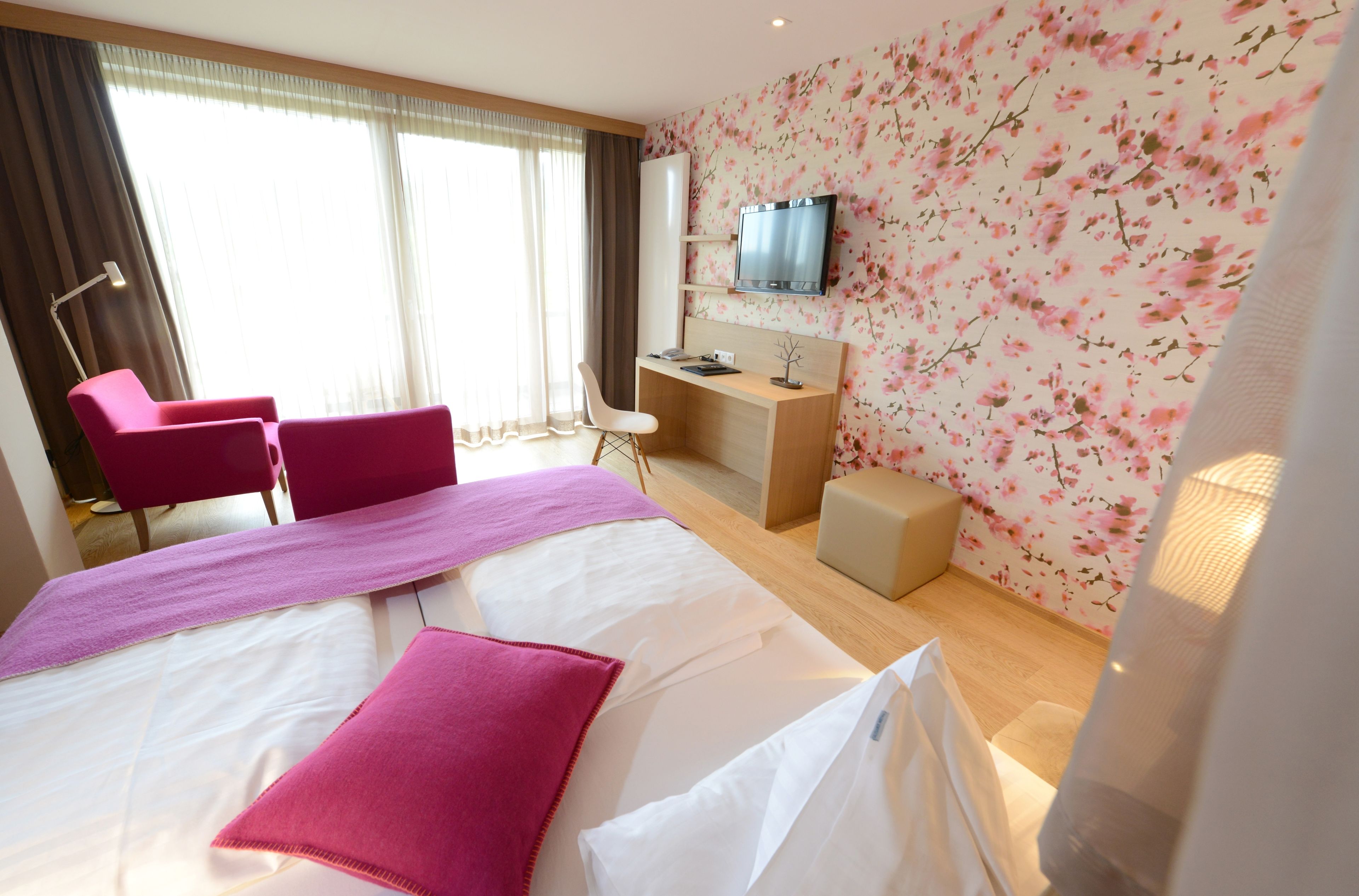 A hotel room with a bed, a desk, a chair, a TV, and a window with curtains.