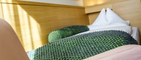 A bed with green and white pillows, a wooden headboard, and a painting on the wall.