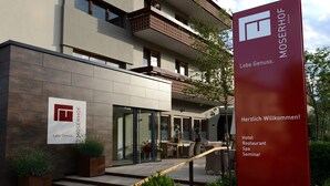 Een moderne hotelentree met een glazen gevel, terrasstoelen en een rood welkomstbord.