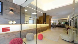 Een modern interieur met een receptiebalie, zithoek en een grote spiegel die de ruimte weerspiegelt.