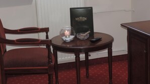 A room with a wooden chair, a small round table with a book, a candle, and a remote control. - Kaiser Franz Josef (Millstatt)