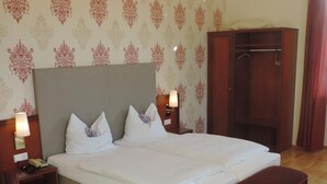 A neatly made bed with white linens, two bedside tables with lamps, a wooden bench, and a wardrobe. - Kaiser Franz Josef (Millstatt)