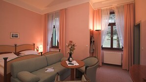 Une chambre d’hôtel avec un lit, un canapé, une petite table avec un vase et une fenêtre avec des rideaux.