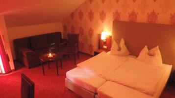 Une chambre d’hôtel comprenant un lit, un canapé, une chaise, une petite table et une table de chevet avec une lampe.