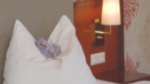 A bed with a white pillow and a small purple flower. - Kaiser Franz Josef (Millstatt)