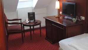A hotel room with a bed, a desk with a television, a chair, a small table with a candle, and a skylight. - Kaiser Franz Josef (Millstatt)