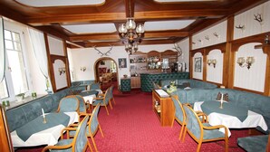 A restaurant with green upholstered booths, wooden tables, and a red carpeted floor. - Kaiser Franz Josef (Millstatt)