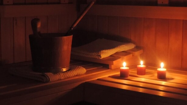 A sauna with a wooden bench, a bucket, and three lit candles. - Kaiser Franz Josef (Millstatt)