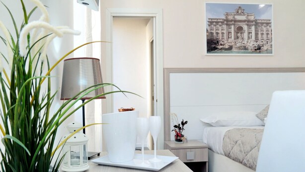 A hotel room with a bed, a bedside table with a lamp, a potted plant, and a framed picture on the wall. - Relais Incantesimo Vaticano (Rome)
