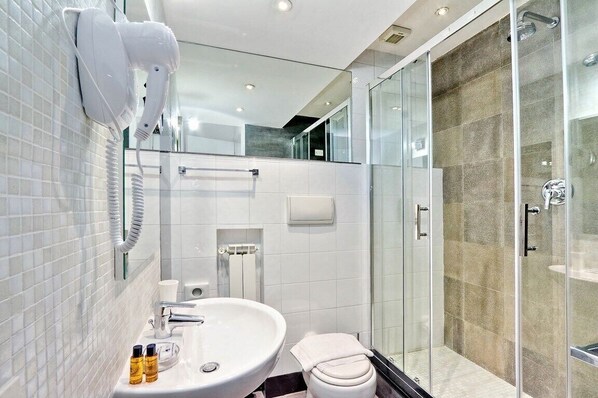 A modern bathroom with a glass-enclosed shower, a white sink, and a hairdryer mounted on the wall.
