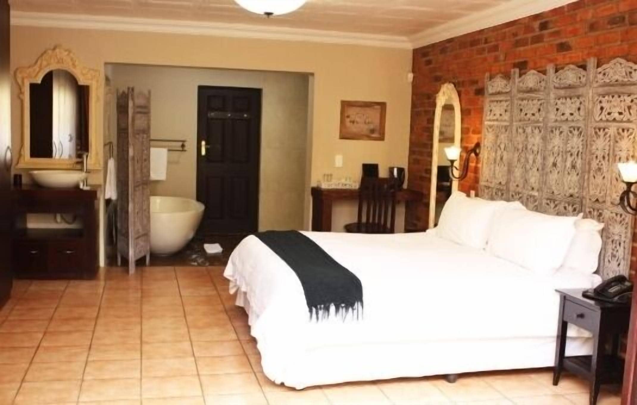 A bedroom with a large bed, a desk, a chair, a bathroom with a bathtub, and a mirror.