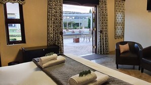 Habitación de hotel con cama, dos sillones, televisor y vista al patio exterior.