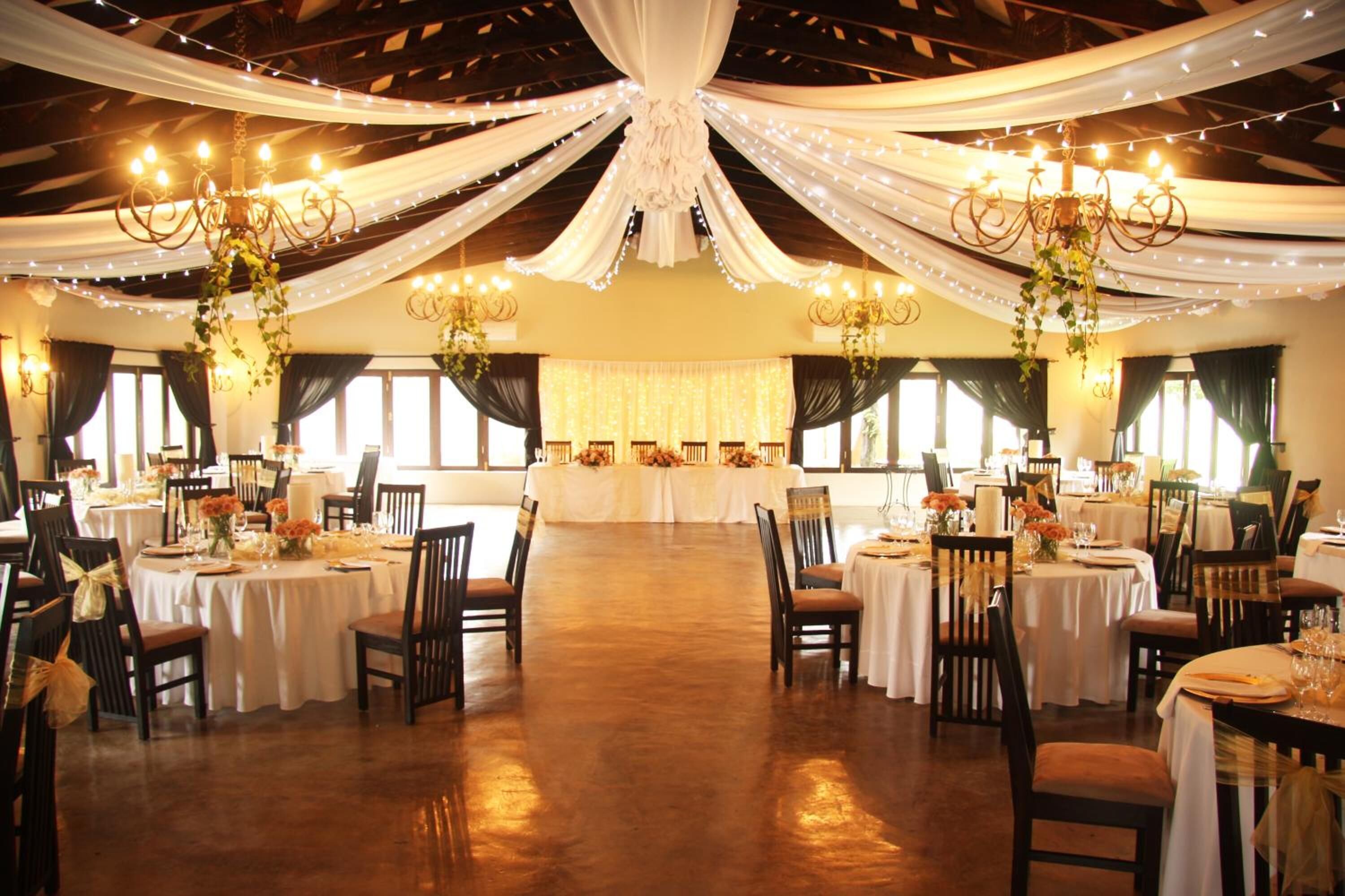 Une salle de banquet avec des tables rondes, des lustres et des tentures.