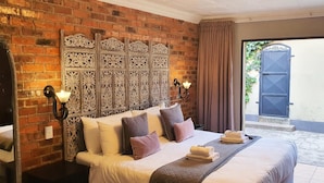 Habitación de hotel con pared de ladrillo, un cabecero decorativo, una cama con almohadas, una mesita de noche y vistas a un espacio exterior.