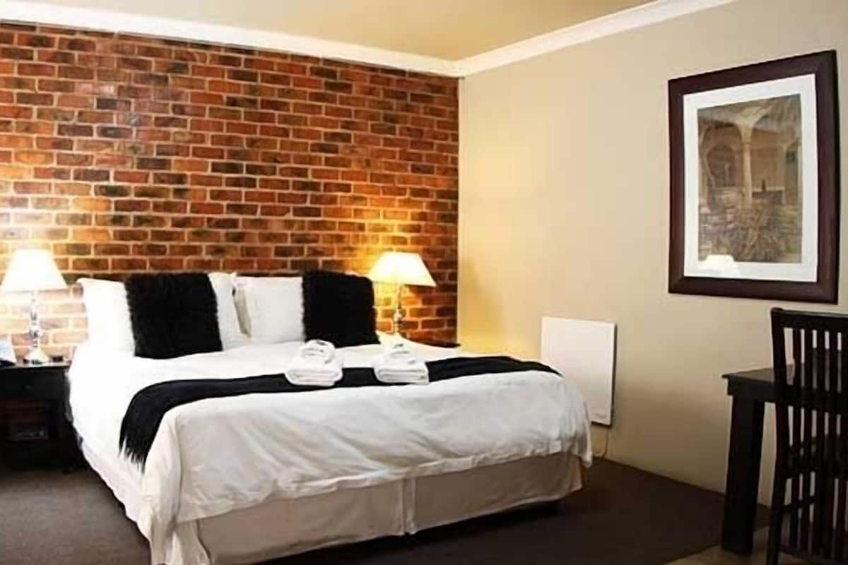 Une chambre d’hôtel avec un mur d’accent en briques, un lit avec une literie blanche, deux lampes de chevet, un tableau encadré au mur et une petite table avec une chaise.